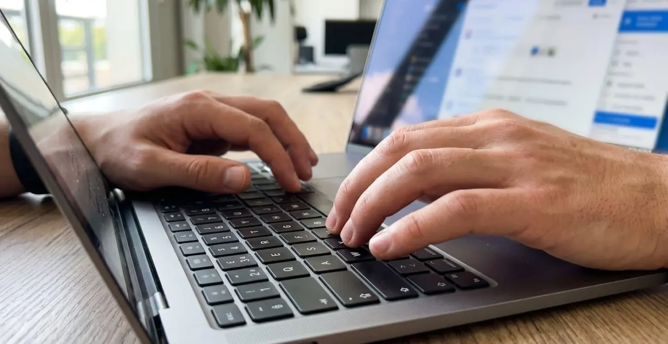 Gros plan sur des mains tapant sur un clavier d'ordinateur portable moderne, écran complètement flouté en arrière-plan